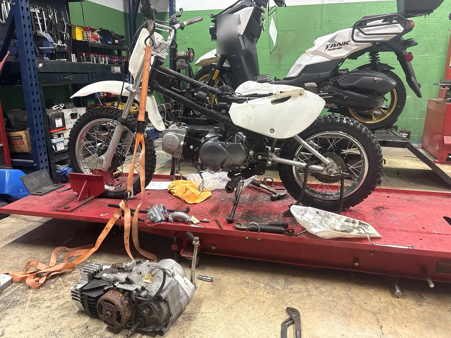 Dirt bike engine replacement in progress with the removed engine in the foreground